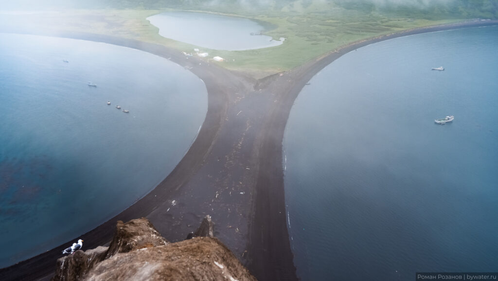 Корабли на спокойной воде у черного пляжа.