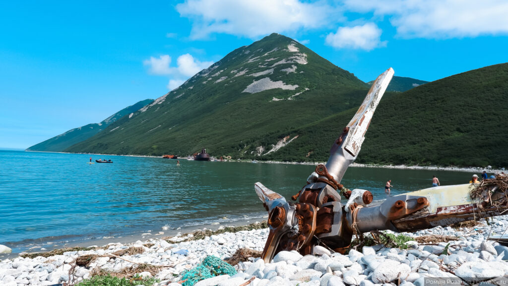 Коряга и останки корабля на берегу среди гор.