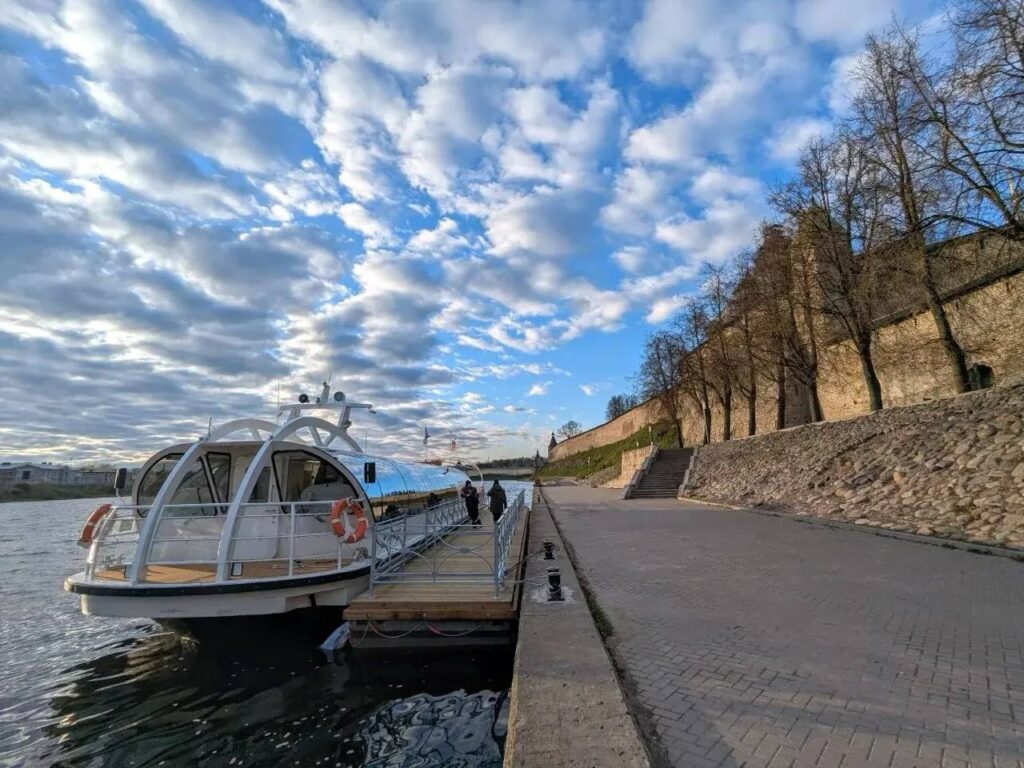 Современный речной теплоход у причала на фоне облачного неба.