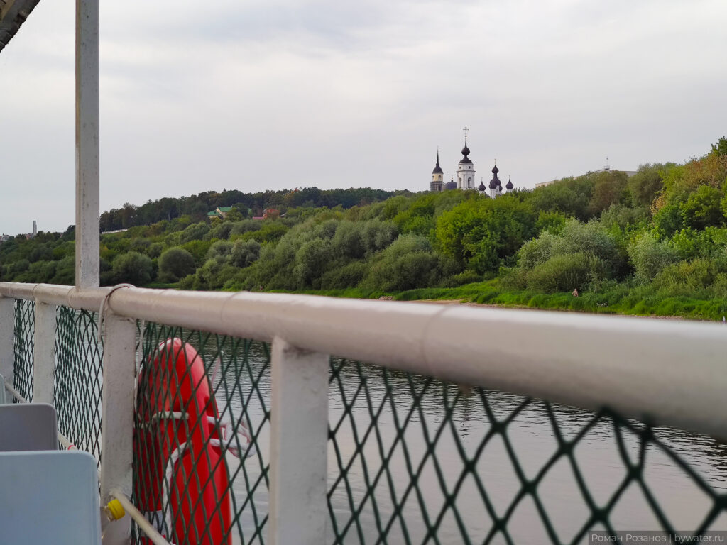 Речной теплоход на фоне зеленого берега и церкви.