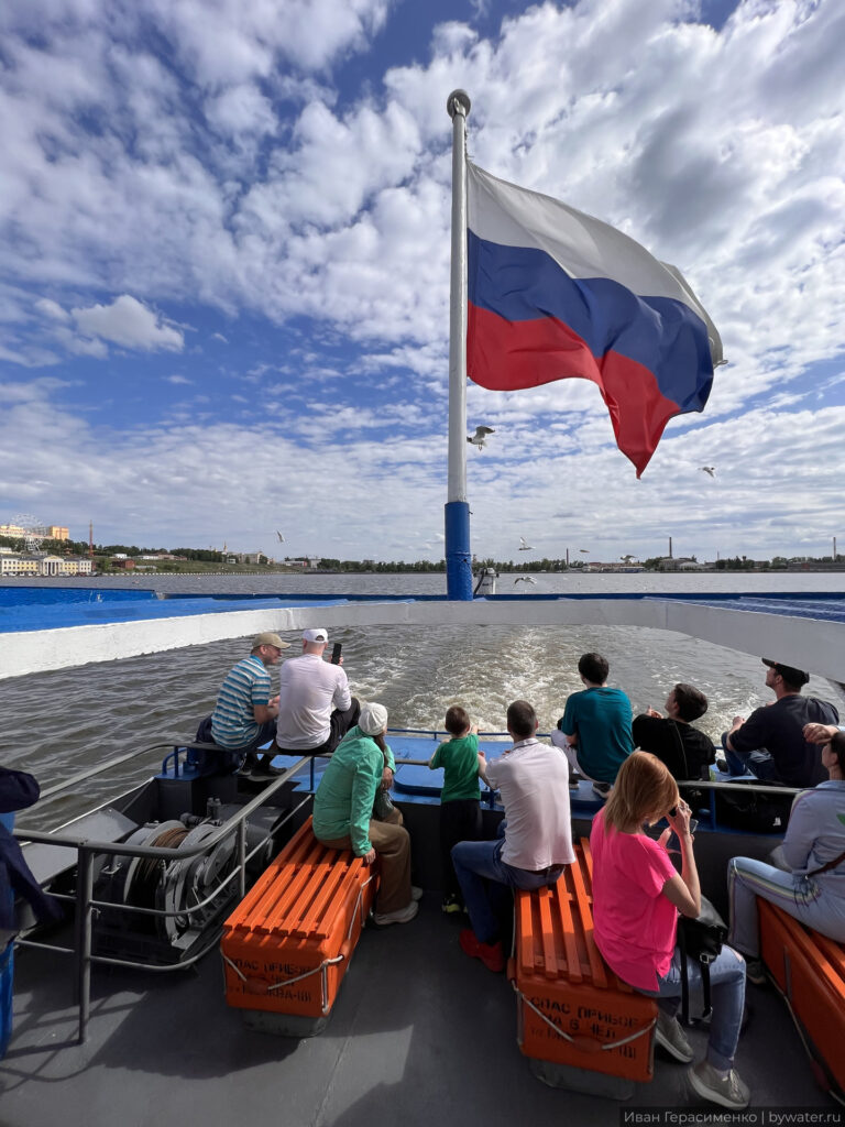 Пассажиры на теплоходе с российским флагом на реке.