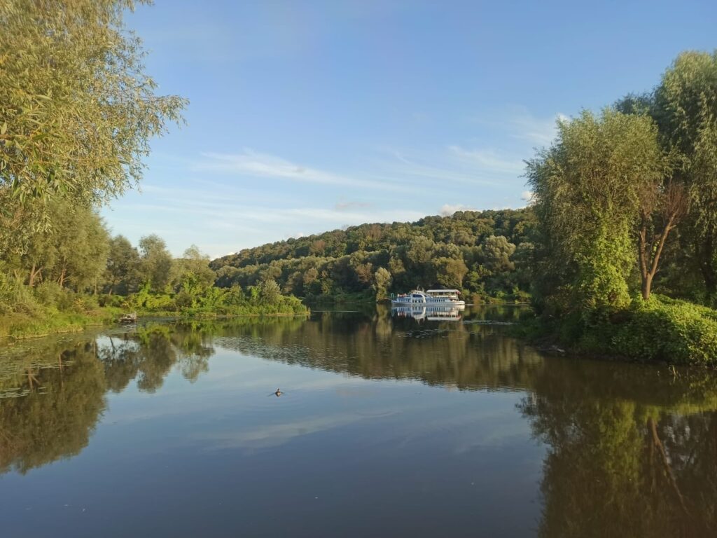 Речной теплоход на спокойной воде с деревьями.