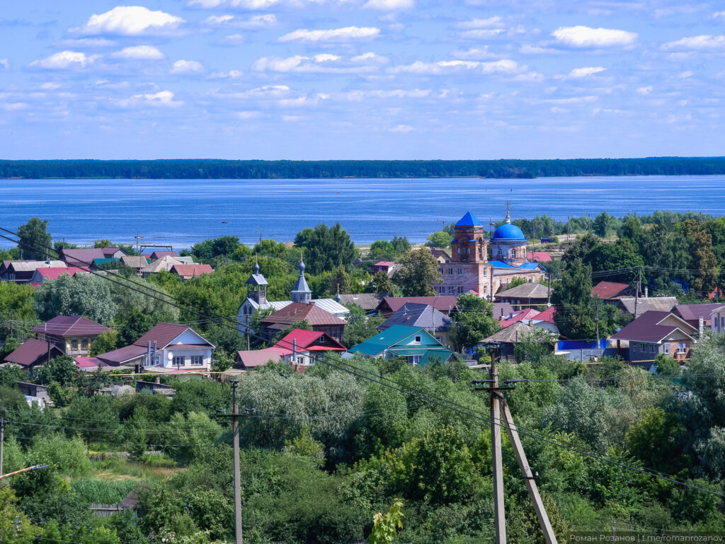 Городская панорама у реки с церковью и домами.
