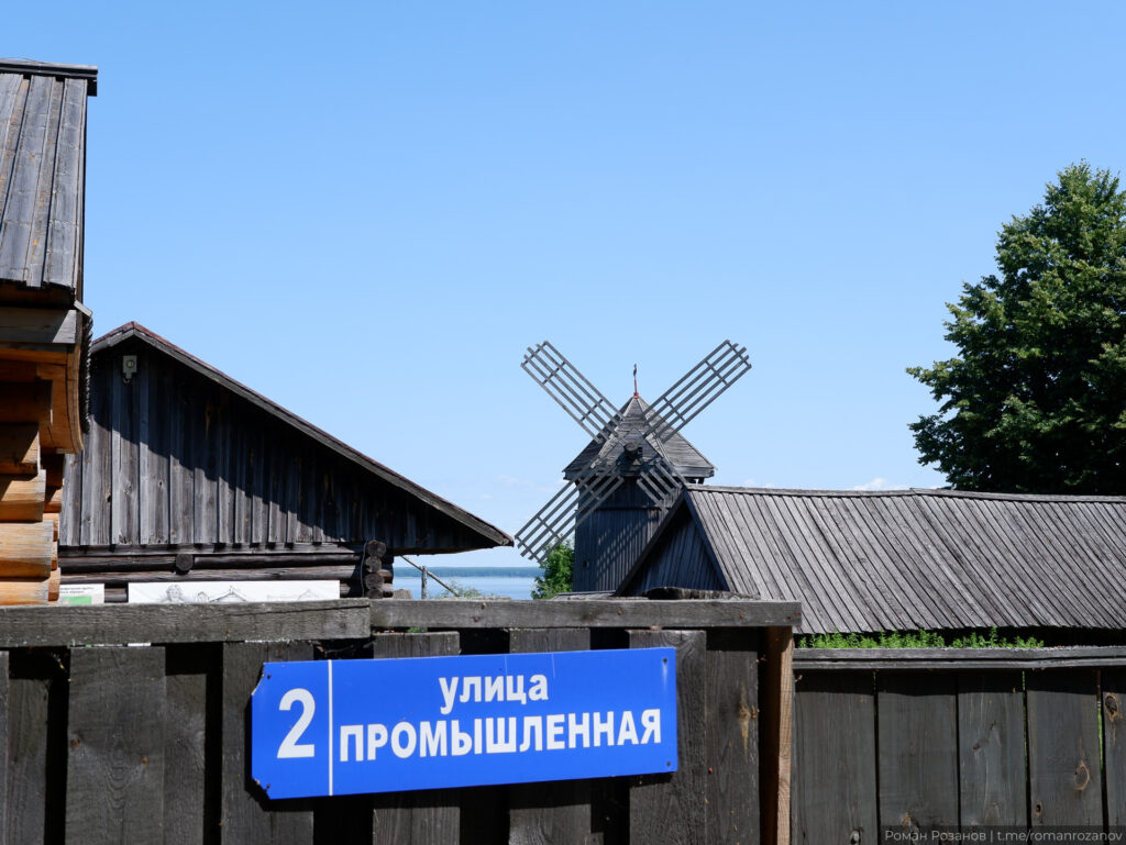 Деревянная мельница на фоне домов и синего неба.