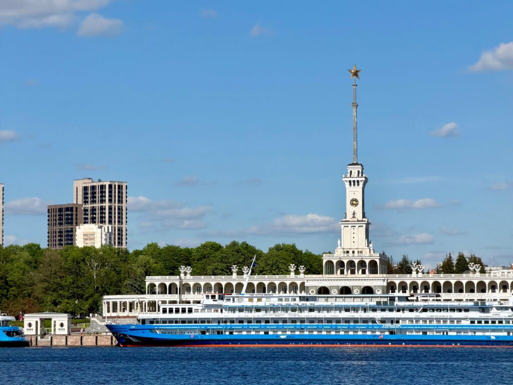 Речной теплоход у причала с высотными зданиями на фоне.