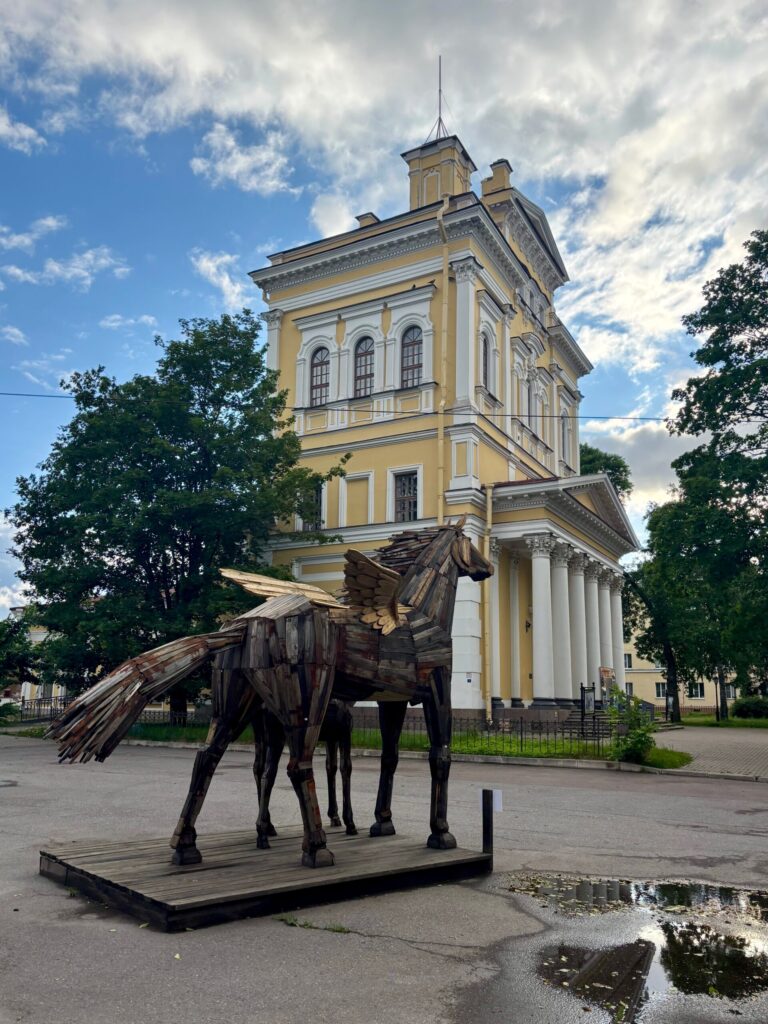 Деревянная скульптура лошадей на фоне желтого здания.